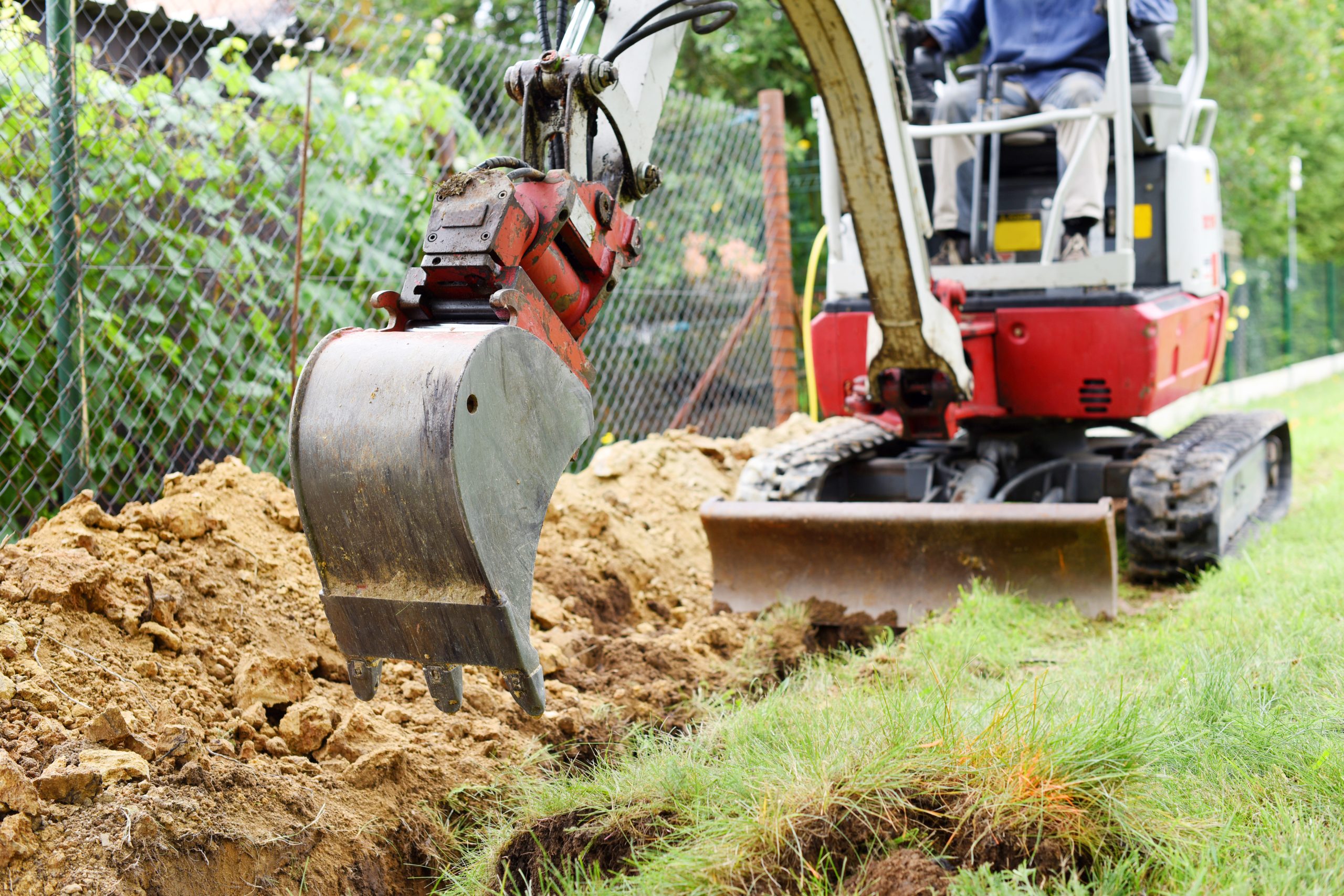 Workman using a mini digger to excavate a hole in the garden. Czech republic, Europe.